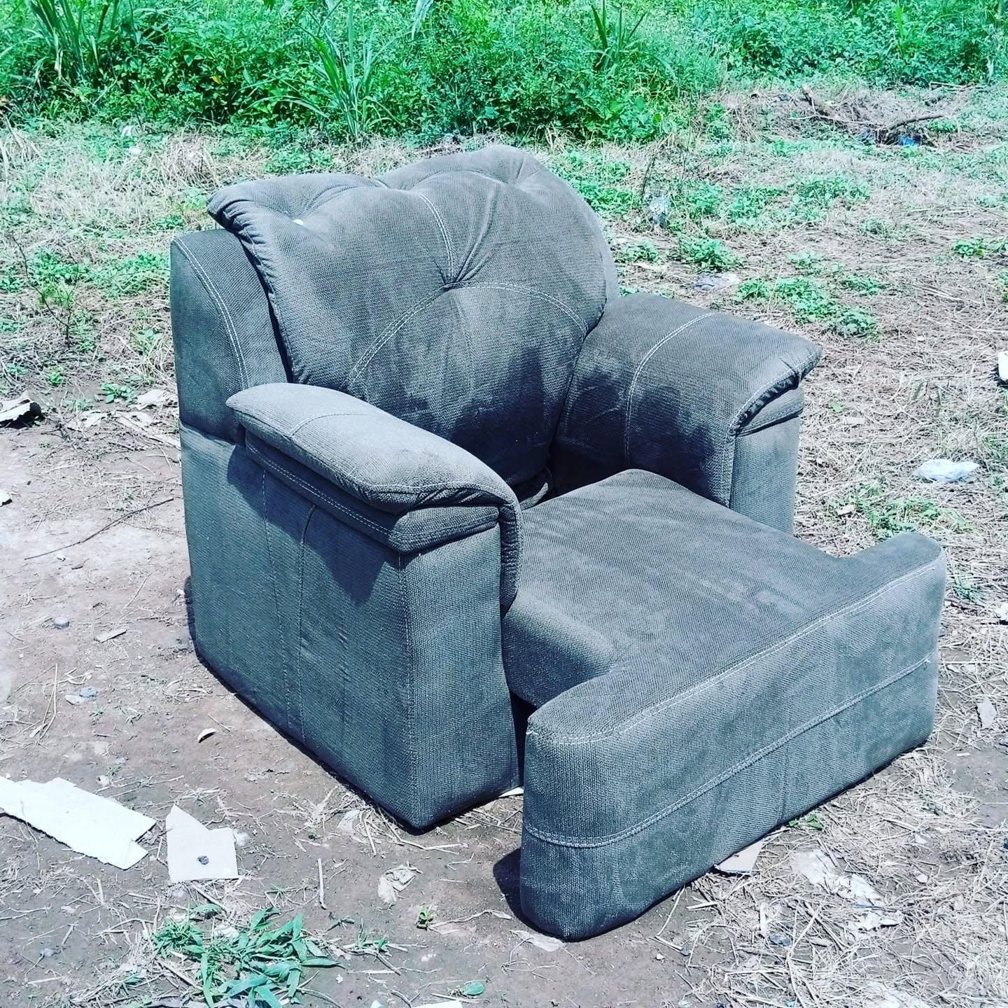 Charcoal-grey padded armchair with broad cushioned arms and contrast stitching, photographed outdoors at the workshop