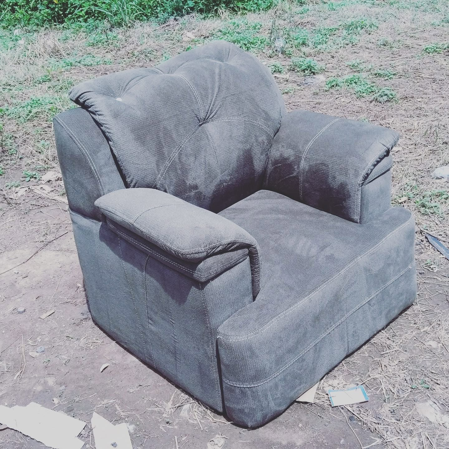 Angled outdoor workshop view of a charcoal-grey padded armchair with rounded back cushions