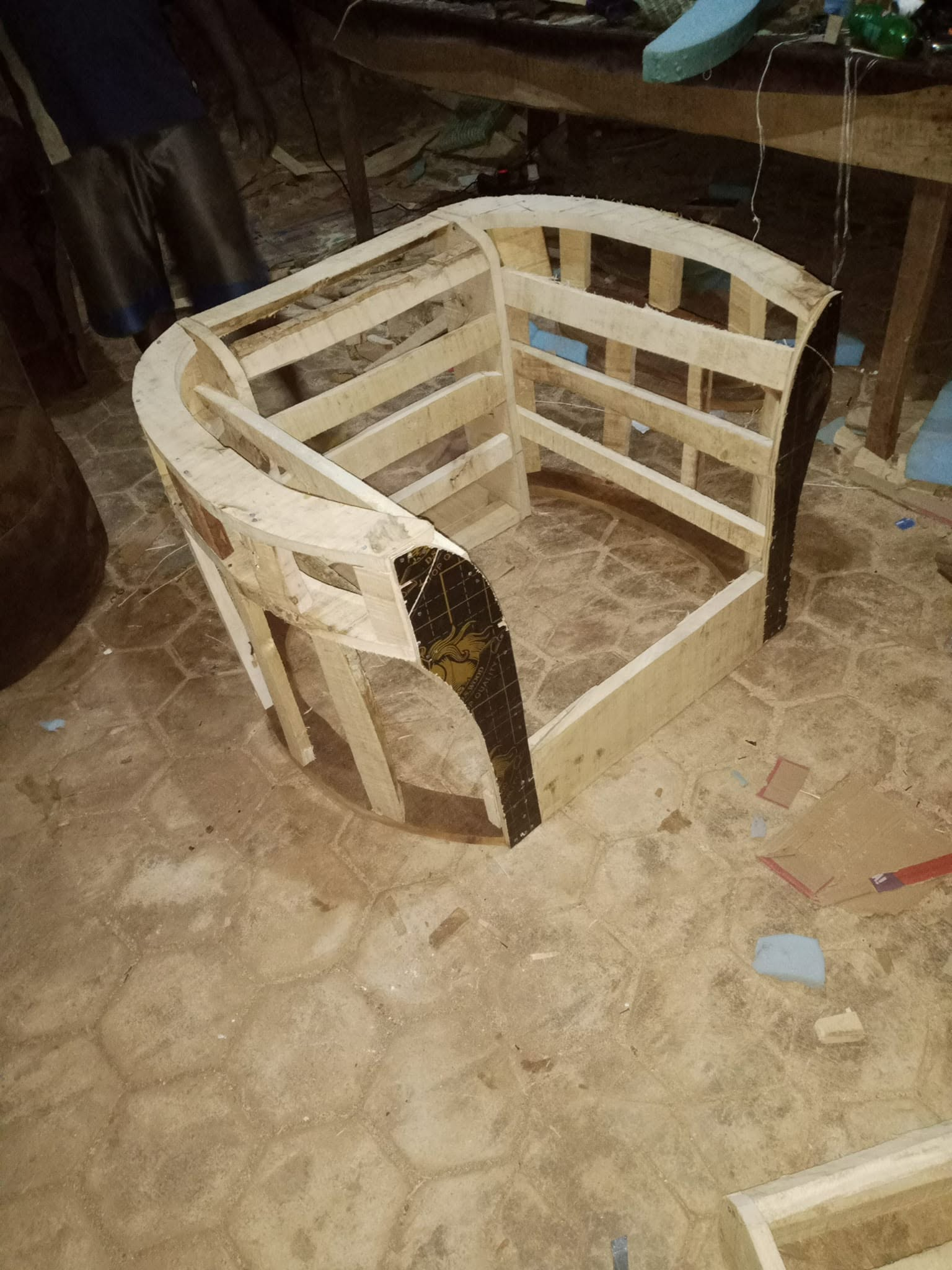 Curved wooden seating frame with open base and arm structure in the workshop