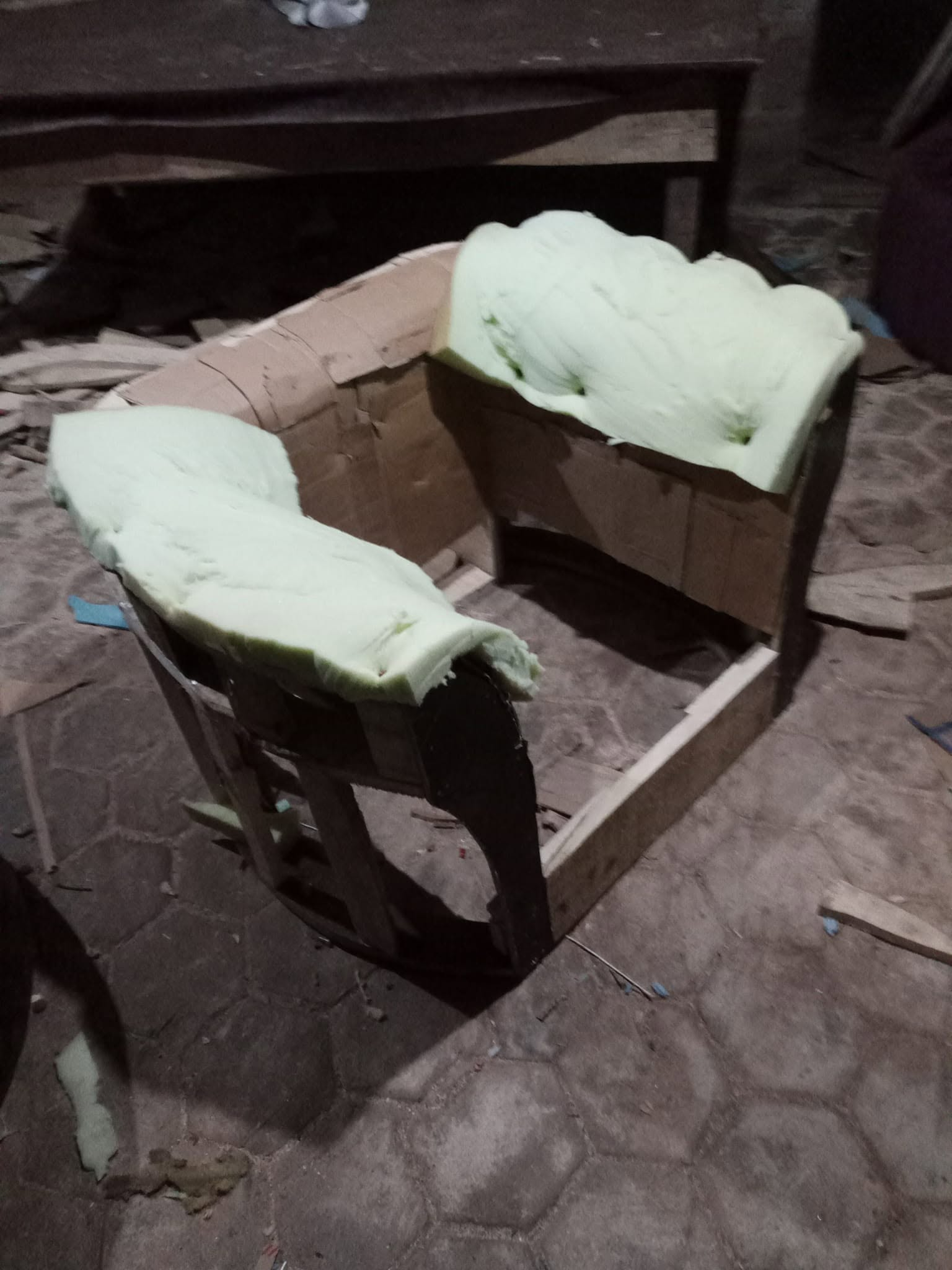 Curved seating frame with pale foam placed around its arms and back in the workshop